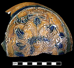 German brown stoneware Bartmann bottle with applied medallion and cobalt blue painting under the glaze. The medallion bears the date 1593, the initials RRK and depicts a double-headed eagle. This vessel would have been 14 to 15” in height. Sherd discovered off of Kent Island, possibly from disturbance of a now-submerged well from the William Claiborne Site, 18QU300. Photo courtesy of Darrin Lowery.