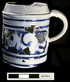 Gray-bodied salt glazed stoneware straight-sided tankard  with applied AR medallion and engraved (incised) foliage outlined in cobalt-blue under the glaze. Cordoned rim. This medallion stands for British monarch Queen Anne (1702-1714).  Vessel date 1702-1714, from 44YO205 John Bates Site. Photo courtesy of the Colonial Williamsburg Foundation. Artifacts from private collection.