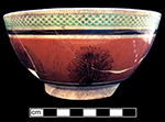 Common-shape pearlware bowl with mocha decoration against orange slip.  Green-glazed diamond rouletted rim. Vessel shows damage from burning. 6.25” rim, 3.125” vessel height.