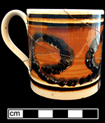Creamware mug,  common cable on orange slip, brown rim and base banding. 3.5” rim diameter, 3.5” vessel height.