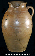 Buff bodied salt glaze stoneware handled jar with incised parallel lines on shoulder. Iron wash on interior and exterior.  Strap handle. Three gallon capacity. Vessel height: 15.00”, Vessel rim diameter: 5.75”, Vessel base diameter:  6.00”, Vessel V-19 from 18MO609.