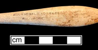 Bone handle with teardrop shape toothbrush with wire drawn attachment and copper alloy staining on back. Stamped on front: “England” near stock and “Hochschild Kohn & Co. Baltimore” and “Drawn Wire/Sterling/Silver Wire” on handle. 18BC92