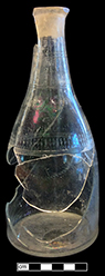 Colorless soda lime glass taper shaped decanter.  Wheel engraved swag motif. Cut flutes along neck. Empontilled flat base and ground interior bore. 9” vessel height; 3.75” base diameter; 1 2/8” lip diameter. Possibly Amelung New Bremen Factory 1784-1795 (see McKearin and McKearin 1989: Plate 42). Similar to decanter shown on right from a private collection. 18BC27-F30