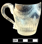 Colorless leaded mug with cut flutes along base and cut ovals and engraving along rim.  Vessel has a strap handle. Rim diameter: 2.75”, Base diameter: 1.75”, Vessel height:  2.50”. Lot: 15, Provenience: 1H1.611.1, Privy Stratum 4. 18BC38