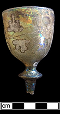 Gold stained glass cordial with white enameled grape and leaves motif. Rim diameter:  1.50”, Vessel height: 3.50”(based on another example in the feature). Lot: 100. 18BC80