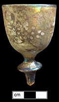 Gold stained glass cordial with white enameled grape and leaves motif. Rim diameter:  1.50”, Vessel height: 3.50”(based on another example in the feature). Lot: 100. 18BC80