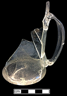 Colorless soda lime glass mug with applied strap “arc” or D-shaped handle. Cylindrical form with flaring base and rough pontil.  4.5” vessel height; 3.25” base diameter. 18BC27-F26