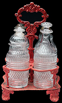 Contact molded leaded glass caster or cruet; blown three mold. Base diameter: 1.50”. On right, blown molded caster set similar to vessel at left. Has two shakers with period brass caps, and a mustard and cruet bottle, with bull's-eye finial stoppers. Sheet-iron and Britannia stand. Made by Boston & Sandwich Glass Co. and others. 1825-1835. Casters 4 1/2" to 5". Private collection. 18BC79