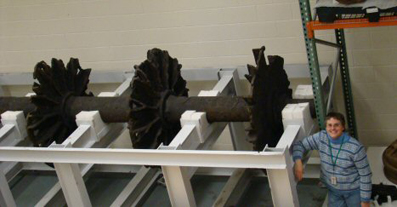 JPPM staff member standing alongside paddle wheel component, which is encased in a metal frame for storage.