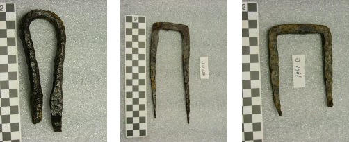 Figure 1 Corroded and waxed iron U-shaped staple or fastener with black surface and gray corrosion patches next to centimeter scale bar on gray background, showing deteriorated condition before conservation treatment.