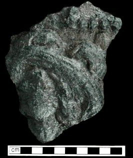 Figure 1 Iron fireback on a back background.  Image on the fireback includes a seated woman holding a lance and a lion rampant holding a sword and bundle of arrows.  Both figures are shown inside city walls with the words 