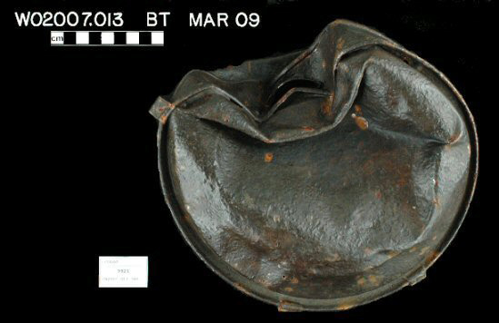 Figure 1 Archaeologically recovered Civil War canteen with collapsed crushed body showing dark patina, orange rust spots, and damaged spout attachment against black background.