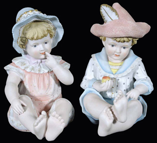 Painted porcelain figurines of a toddler girl in a bonnet and a toddler boy wearing a feathered cap.
