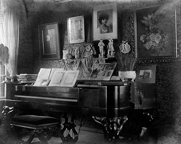 Piano with bench and sheet music. The piano is topped with figurines, clocks, plants and photographs.