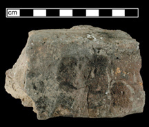 Side view of a partial brick with the imprint of four human fingers.