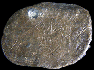 Flat oval shaped lead disc showing close-up of incised grid marks.