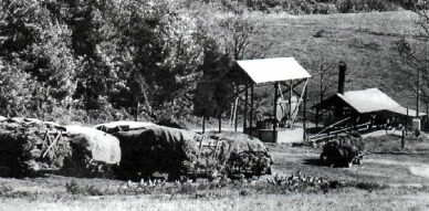 Figure 3 Black and white historical photograph showing iron industrial equipment in a rural setting, with two covered structures among trees and hillside terrain.