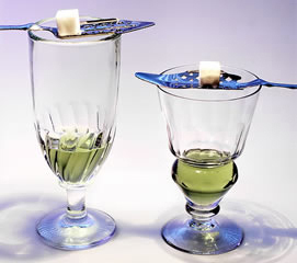 Two stemmed glasses containing absinthe and each balancing a slotted spoon and sugar cube on top.