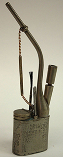 Figure 3 Antique Chinese opium smoking set with curved metal pipe attached by chain to rectangular engraved metal case containing cylindrical storage tubes and small brush tool for pipe cleaning.