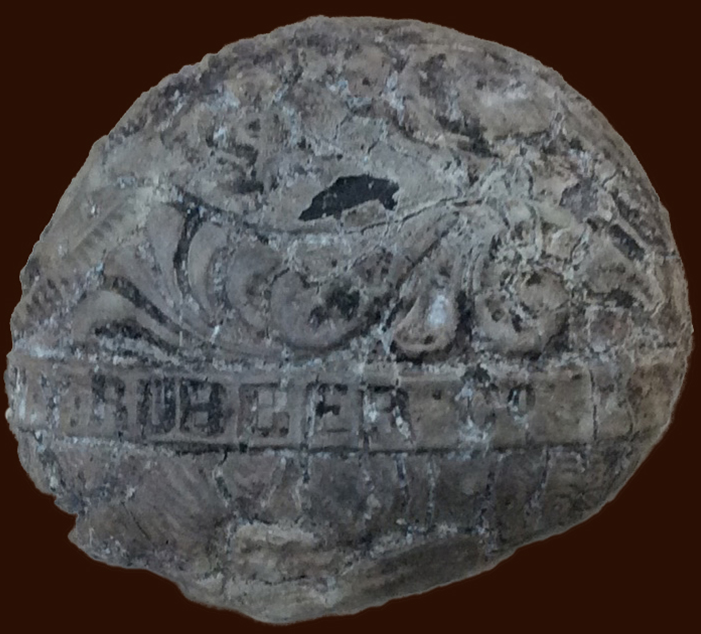 Round grey object with molded floral motif and words 