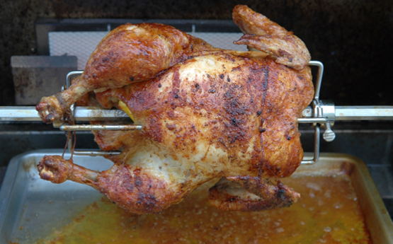 A turkey on a spit roasting over a metal basing pan in an oven.