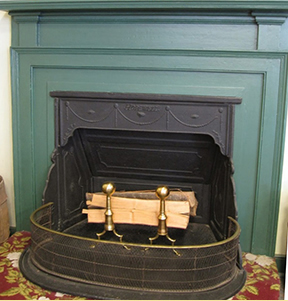 Black cast iron Franklin stove with open paneled doors installed in pale green painted fireplace surround.