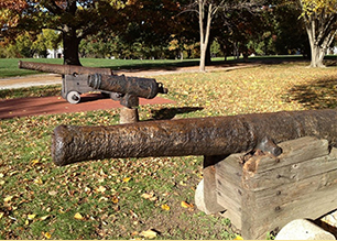 Three corroded historical iron cannons displayed outdoors in park setting.