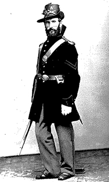 Black and white historical photograph of Civil War officer in full dress uniformbstanding in formal studio portrait pose.