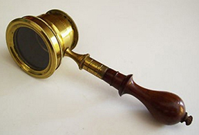 Circular brass lense of a 19th-century flea glass on a wooden and brass handle.