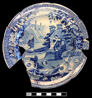 Fragmented and mended dinner plate printed in blue with three women standing and sitting beside a lake.