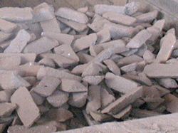 Pile of raw pig iron ingots in rough trapezoidal shape, stacked on ground outdoors