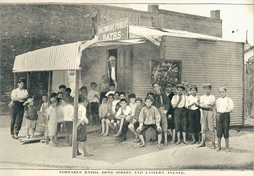 A large group of young men sitting and standing outside a small building labeled 