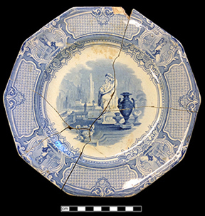 Complete mended plate printed in blue with a classical motif of a woman sitting among Grecian urns.