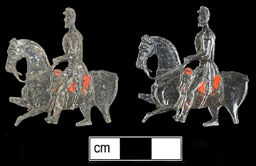 Two lead toy soldiers on horseback with traces of red paint on a black background with a scale bar.