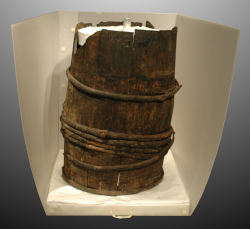Deteriorated wooden barrel displayed in a white archival storage box