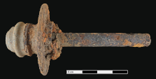 Corroded metal wheel hub and axle photographed against a black background with a metric scale bar