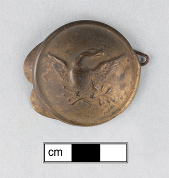 The oval copper alloy boss embossed with a stylized eagle spreading its wings with a
leafy branch and arrows in its talons. This embossed image is not very crisp.