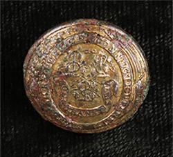 Gold-colored button with round seal centered in a decorative border.