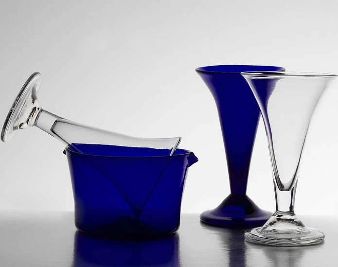 Dark blue glass wine rinser with a colorless wine glass tipped into it for rinsing.  A colorless and a blue wine glass sit to the right of the rinser.