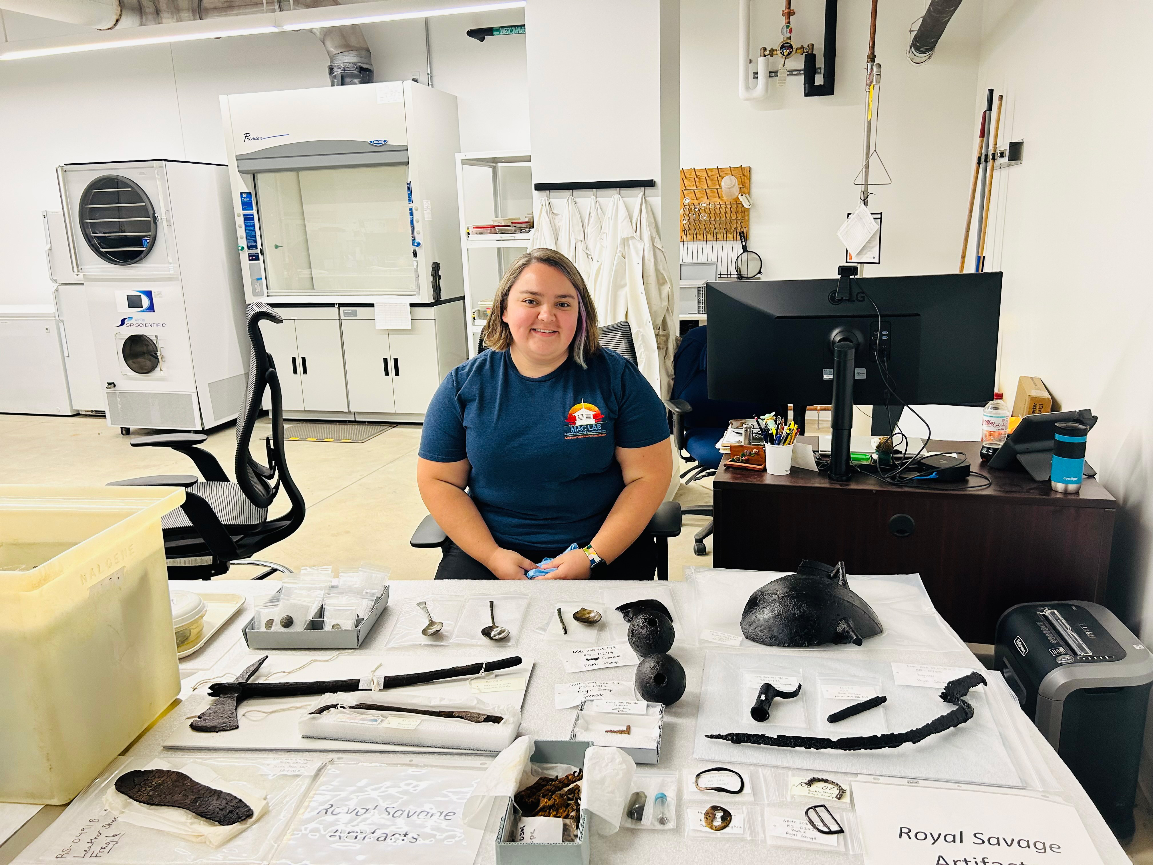 Figure 3 A conservator presents preserved artifacts, including a large hatchet, a shoe sole,
buckles, spoons, and cooking pot fragment.