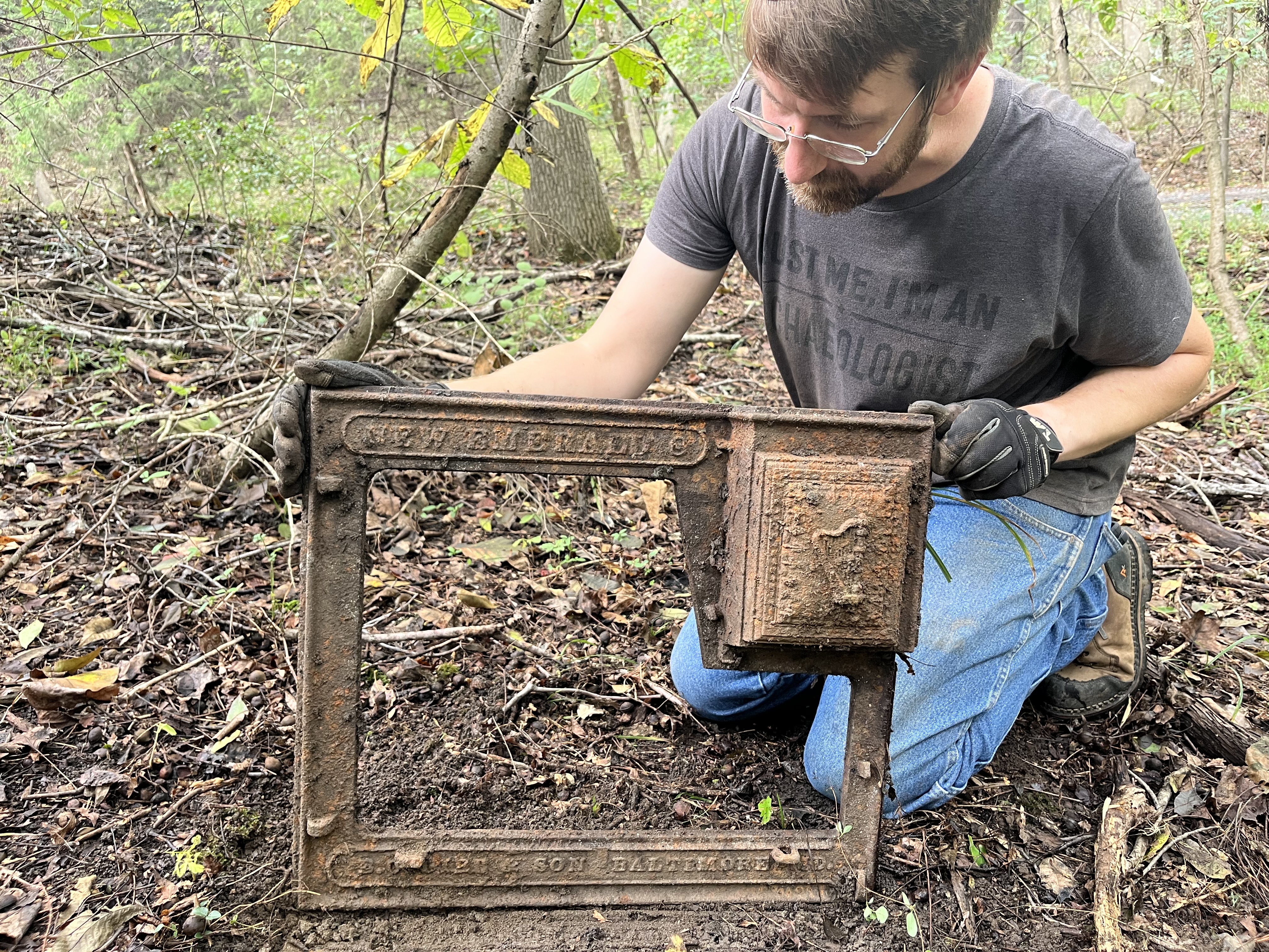 Man kneeling in the woods holding the cast iron side of a cook stove from circa 1880.