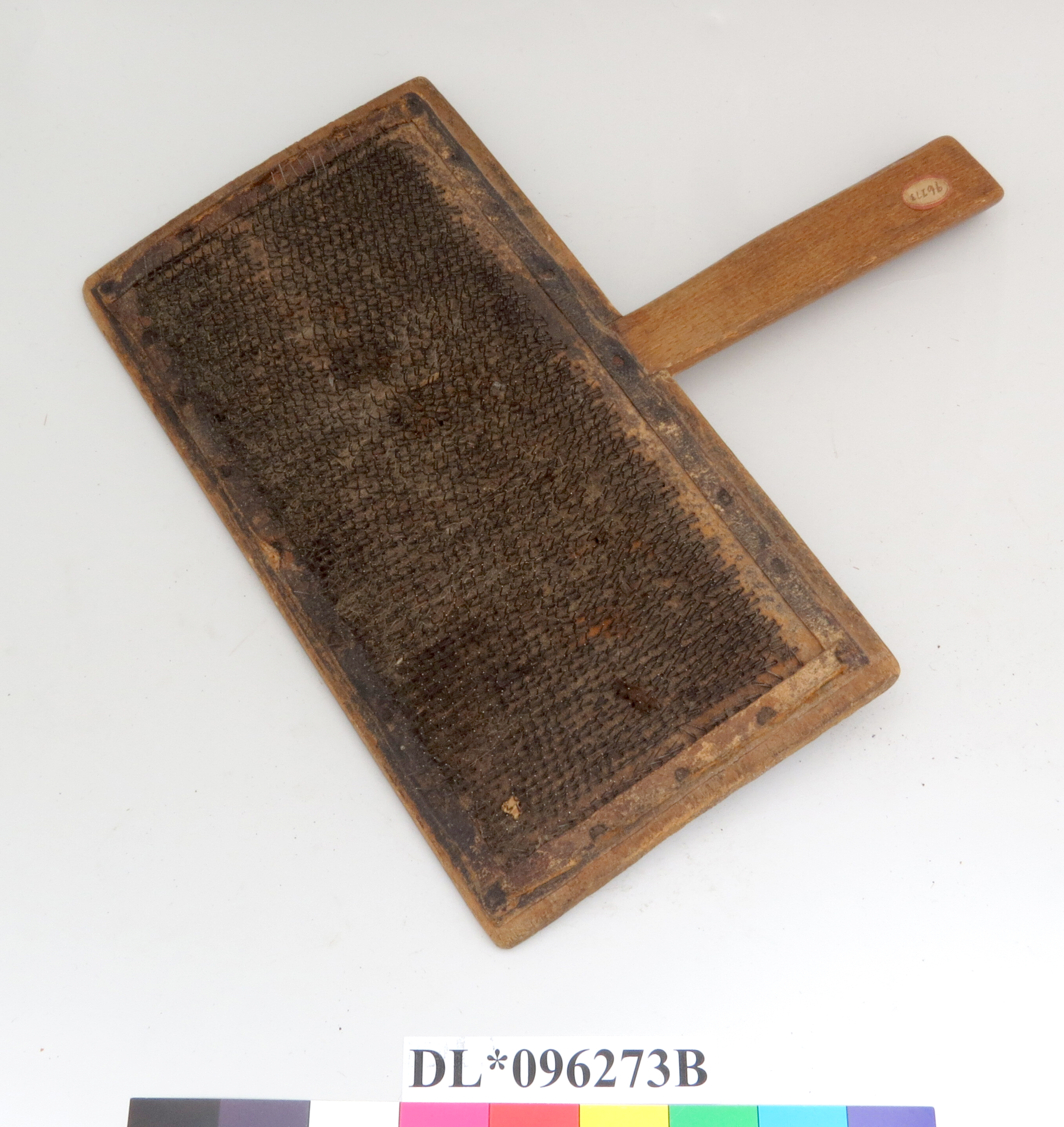 Rectangular flat wood with handle extending from the center of one long side. An array of evenly spaced metal tines protrude away from the wood backing at a 45 degree angle toward the handle.