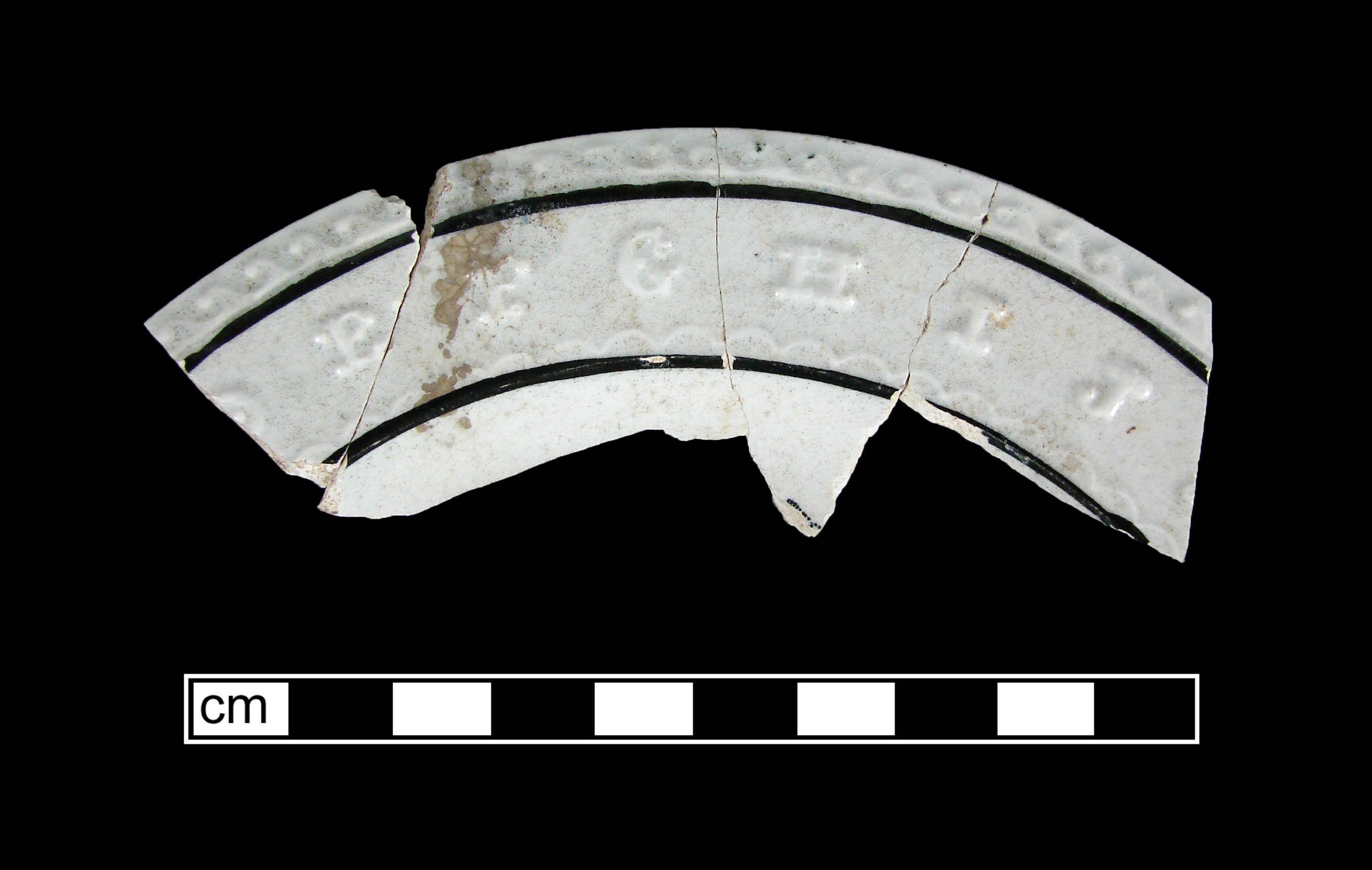 Fragment of white pottery painted around the rim with two black lines.  The alphabet letters E, F, G, H, I, and J are molded on the rim between the black lines.