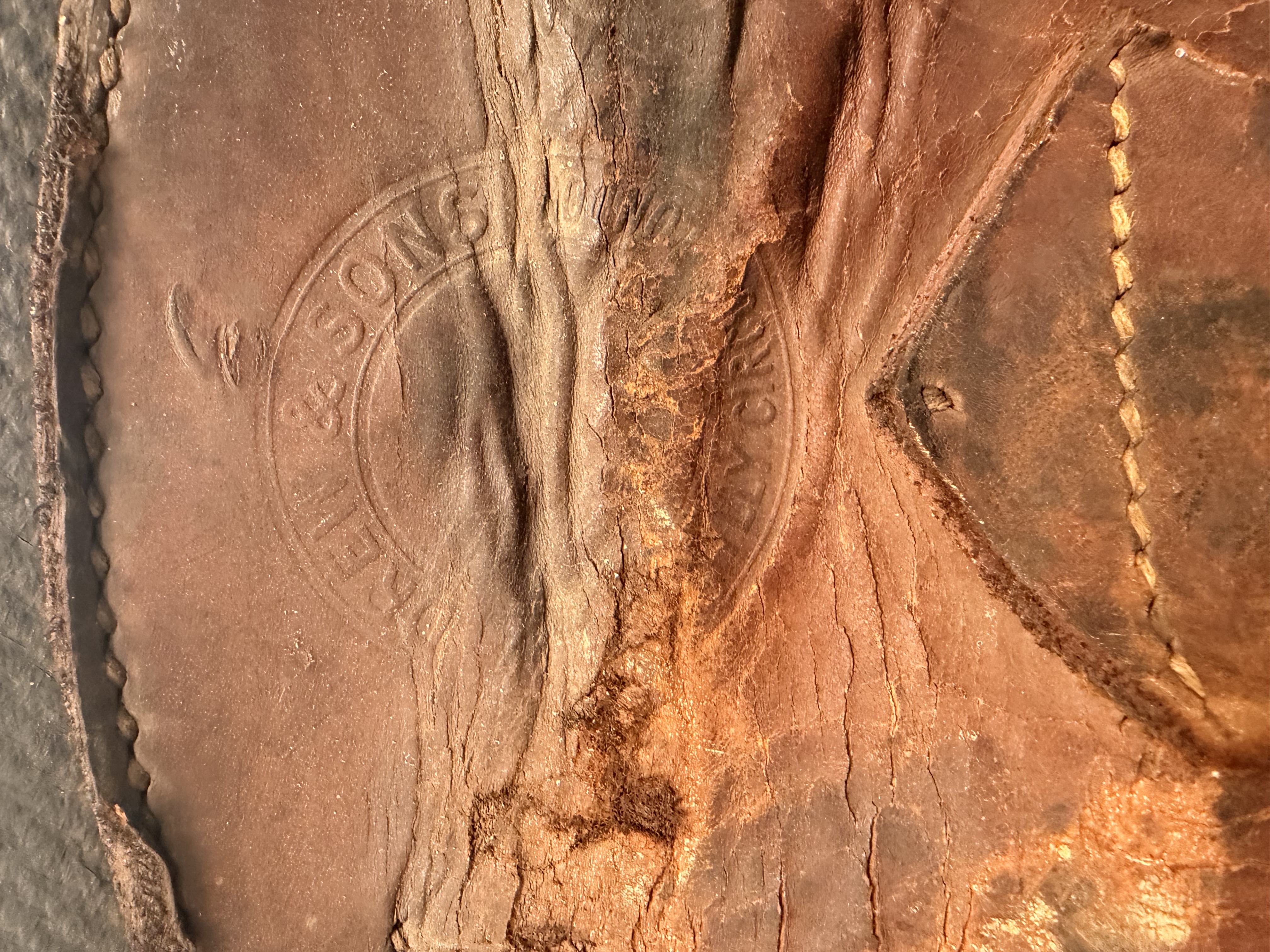 Close-up of the leather strap of a travel trunk displaying the damaged embossed maker's mark 