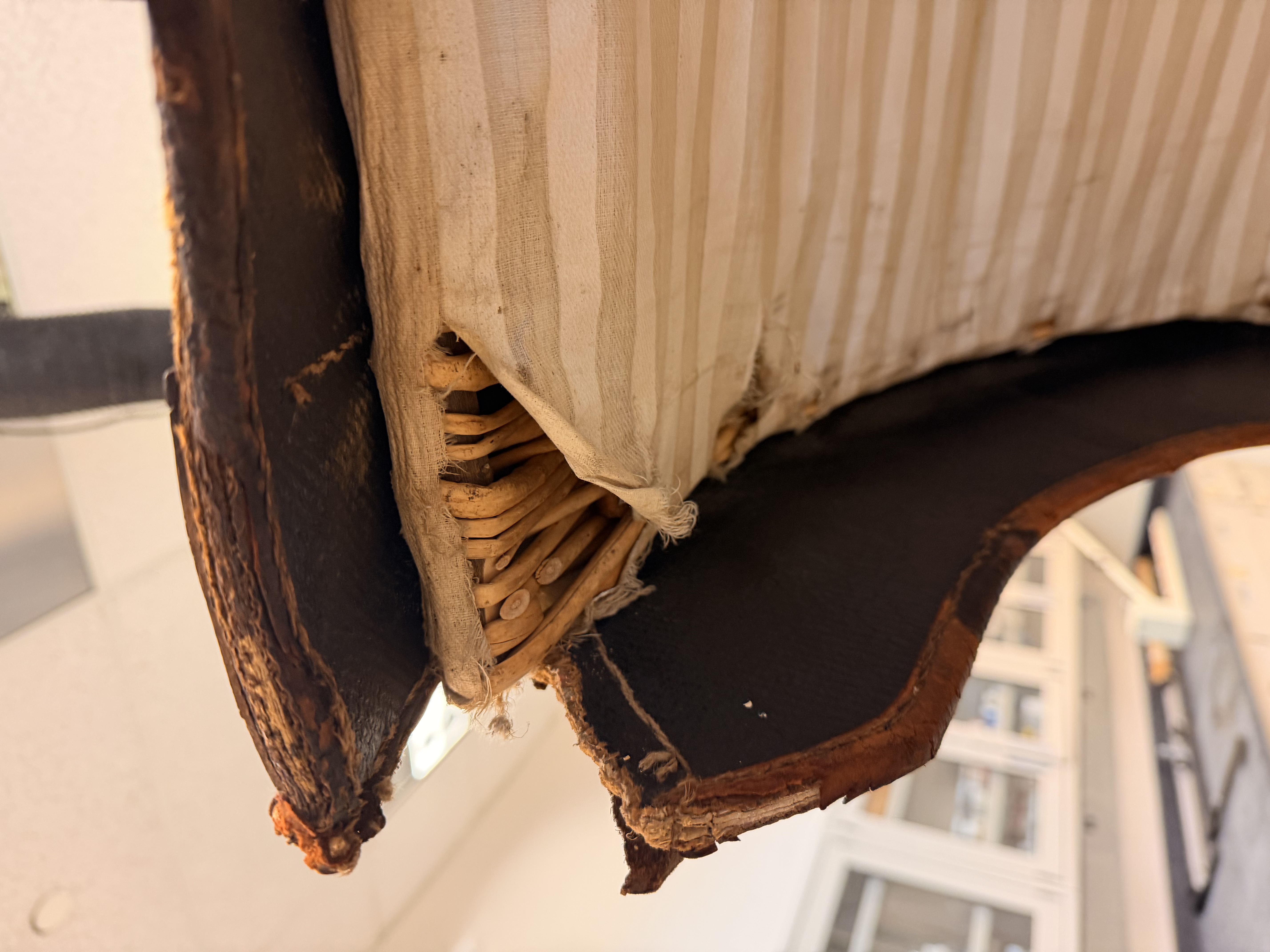 Close-up of a trunk showing an oilcloth cover, wicker base, and striped cloth interior.