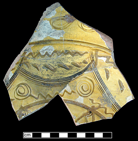 North Devon Sgraffito dish. White slip over red earthenware body, with lead glazed interior. Incised geometric motif. Approximately 12&rdquo; rim diameter. Lots 9, 91, 153, 176. Similar to geometric motif vessel shown in Figure 20 (Outlaw 2002).