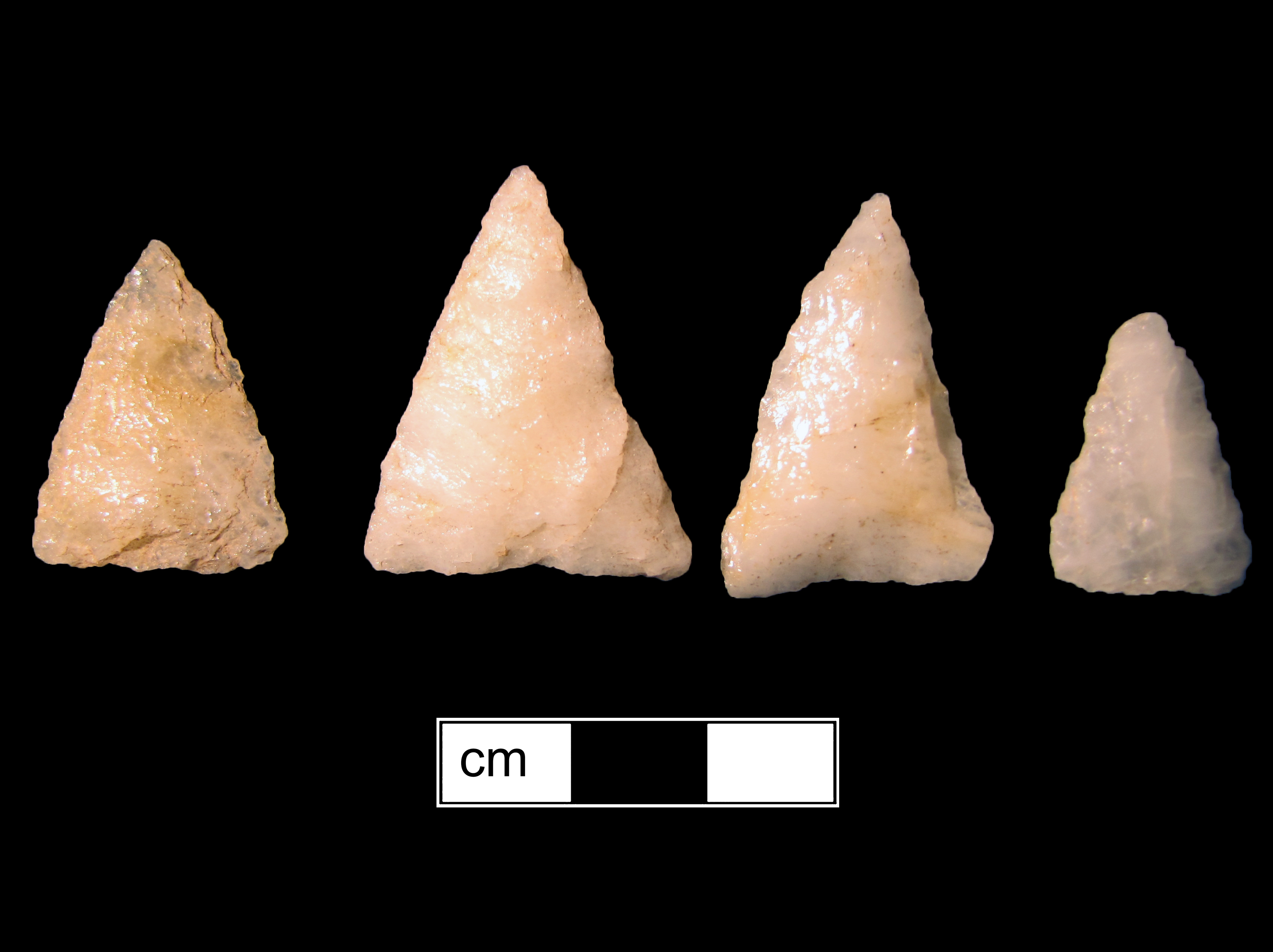 Image of four stone projectile points made of Quartz, Triangular shape, with no stem, Straight blade, and Straight base shape.Archaic triangle type.