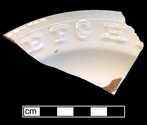 Rim of a refined white earthenware plate with molded alphabet letters and partial printed motif. The wave-like pattern along the outer rim is known as a vitruvian scroll. Rim diameter: 7.50&rdquo;, Vessel 3: 95. 18BC56