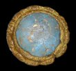 Blue faceted glass jewel in a copper alloy setting with a decorative crimped rim. 