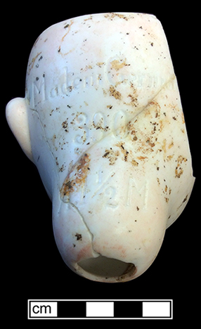 Molded and painted bisque socket head porcelain doll. Impressed on reverse “Made in Germany/390/A 1 ½ M”. Made by the firm of Armand Marseille. Marseille was among the most prolific or German doll manufacturers, beginning production of dolls around 1885 and continuing until around 1930 (King 1981:400). Dolls marked “390”  were usually part of jointed composition dolls. Flattened open area at top of head for placement of hair. 18BC80